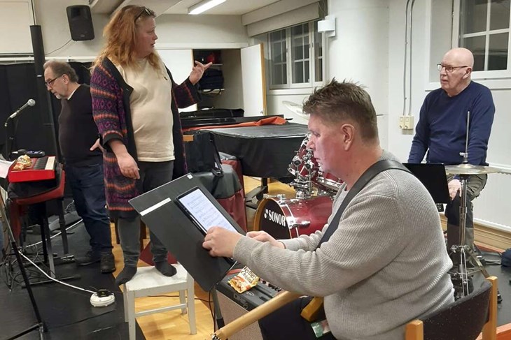 Kristina Öjeskog, ledare för Nåskören, i samspråk med Sten Larsson, bakom trumsetet. Med på bilden är även Calle "Klurik" Johansson och Herry Lehto (närmast kameran) under en gemensam repetition mellan Nåskören och Second Hand Band. Foto: Privat